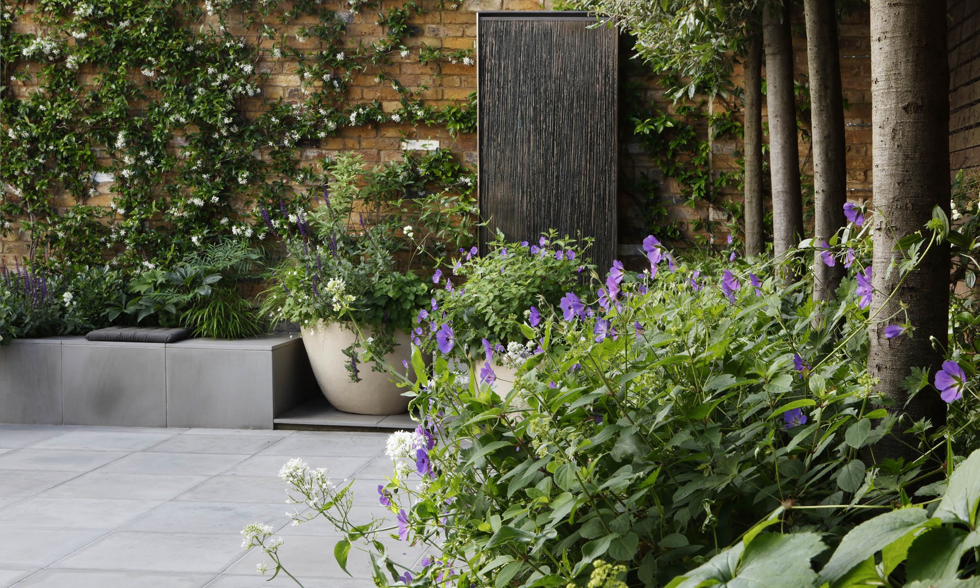 Layered London garden border planted by Shoots & Leaves beside a brick wall and water feature